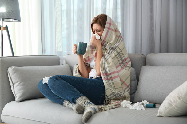 Sick woman wrapped in plaid with cup of hot drink at home. Influenza virus - Foto, imagen