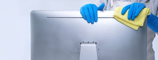 Young woman housekeeper in apron is doing cleaning silver computer screen with blue gloves, wet yellow rag, close up, copy space, blank design concept. - Photo, Image