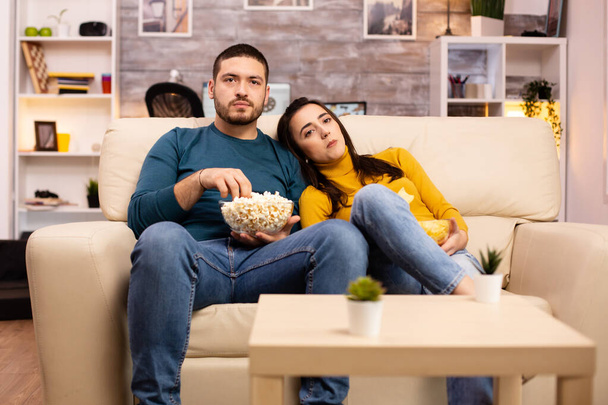 Hermosa pareja en casa comiendo maíz pop y viendo la televisión
 - Foto, imagen