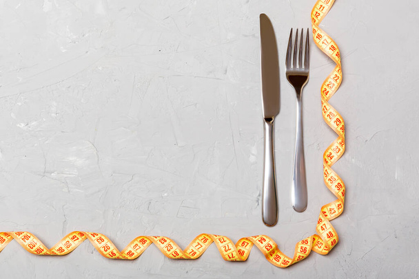 Bovenaanzicht van obesitas concept met vork, mes en gekruld meetlint op cement achtergrond met ruimte voor uw creatieve ideeën. - Foto, afbeelding