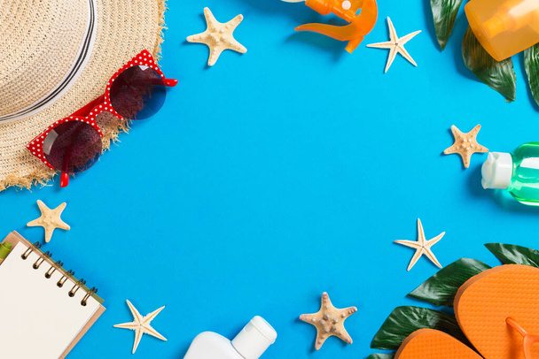 Strandaccessoires mit Strohhut, Sonnenschutzflasche und Seestern auf blauem Hintergrund von oben mit Kopierraum. - Foto, Bild