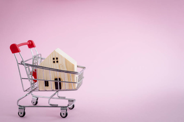 Modelo de casa de madera en el carrito de la compra sobre fondo rosa para la vivienda y el concepto de propiedad
 - Foto, Imagen