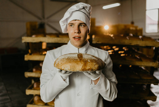 Joven trabajadora feliz en paños estériles sosteniendo galletas recién horneadas en hojalata dentro de la fábrica de producción de alimentos
. - Foto, Imagen