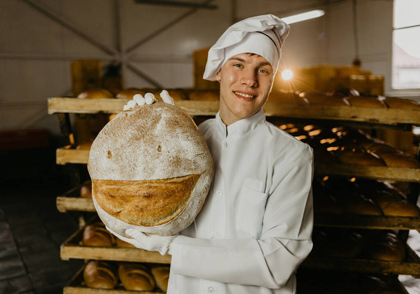 man with fresh bread in his hands, baker in apron and shirt giving hot bread on black background - Foto, immagini