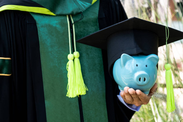 The person in the bachelor uniform  hoding blue piggy bank, Saving money for education plan and retirement fund concept. - Photo, Image