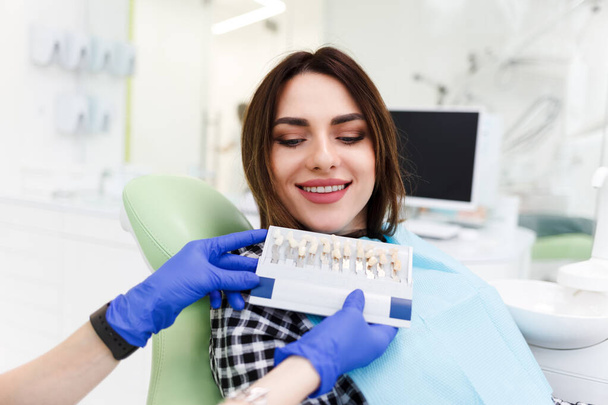 El dentista y su paciente eligen un tono de carillas. Odontólogo médico muestra una paleta con tonos para los dientes
 - Foto, imagen