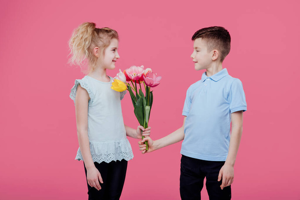 Boy giving flowers to girl pink background - Zdjęcie, obraz