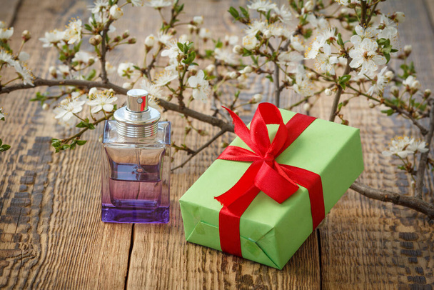 Gift box and bottle of perfume with branches of blooming cherry tree on the wooden background. Concept of giving a gift on holidays. - Photo, image