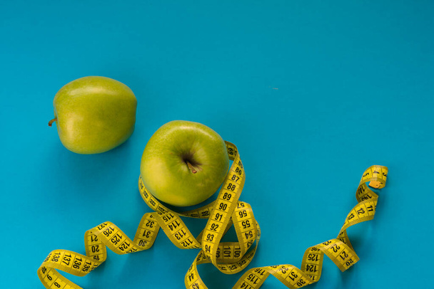 Gele meetlint gewikkeld rond een groene appel op een blauwe achtergrond. Het concept van een gezonde voeding - Foto, afbeelding