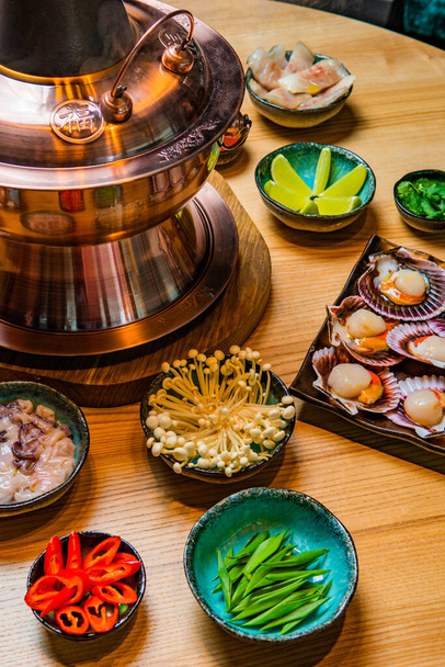 close-up view of traditional asian hot pot and bowls with ingredients on wooden table - Фото, изображение