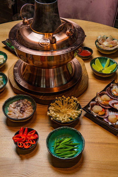 traditional asian hot pot and bowls with ingredients on wooden table - Фото, изображение