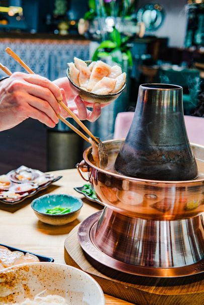 cropped shot of person holding chopsticks with gourmet fish and preparing hot pot meal - Foto, imagen