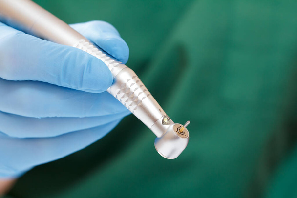 Zahnarzthand in einem blauen Latex-Handschuh mit neuem High-Speed-Dentalhandstück auf unscharfem Hintergrund. medizinisches Werkzeugkonzept. - Foto, Bild