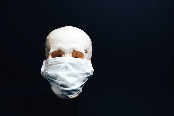 A skull in a medical mask on a black background . The concept of an epidemic , an unknown virus. - Φωτογραφία, εικόνα