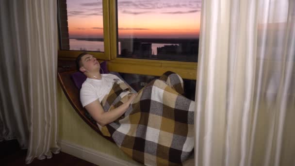 Um jovem ouve música em fones de ouvido. Um homem está deitado numa soleira da janela com auscultadores nos ouvidos. Fora da noite
. - Filmagem, Vídeo