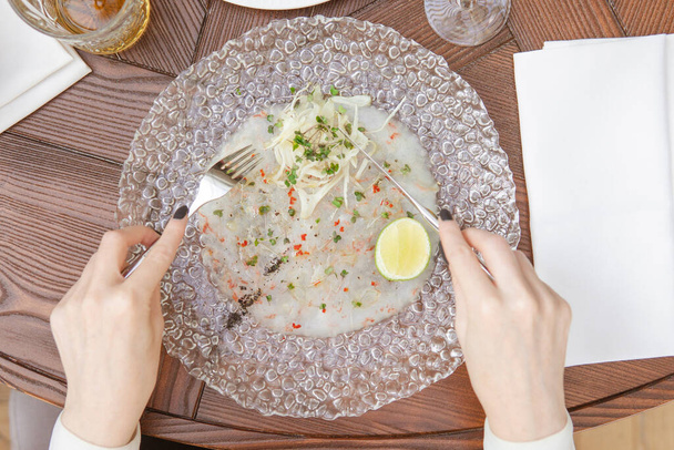 partial top view of person holding fork with knife and eating gourmet dish decorated with lime  - Фото, зображення