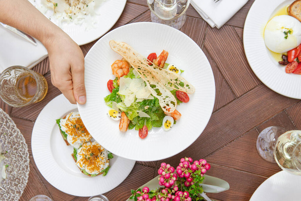 cropped shot of person serving table with delicious dishes and salads  - Zdjęcie, obraz
