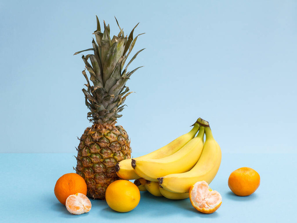 Composição natural de frutas tropicais. Abacaxi fresco, bananas, limão e tangerinas sobre fundo azul
. - Foto, Imagem