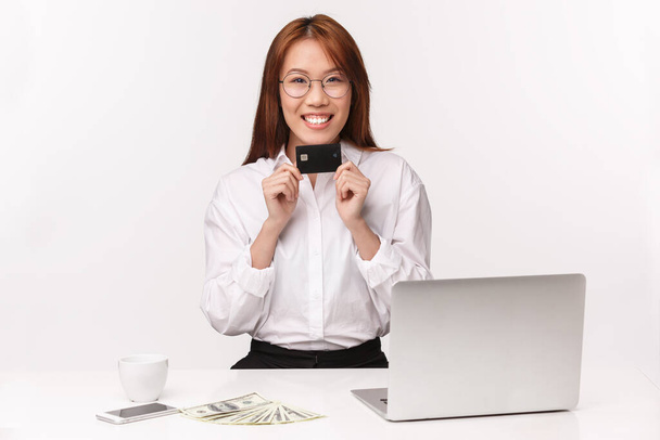 Karriere-, Arbeits- und Unternehmerinnenkonzept. Nahaufnahme Porträt des lächelnden angenehme asiatische Bürodame schlagen Kunden neue Kreditkarte, Bank Assistant Signing Deal, sitzen in der Nähe Laptop Geld und Kaffee - Foto, Bild