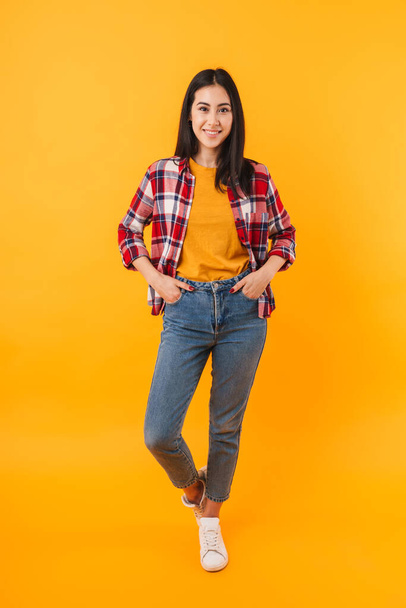 Photo of joyful young woman in casual wear posing and smiling isolated over yellow background - 写真・画像