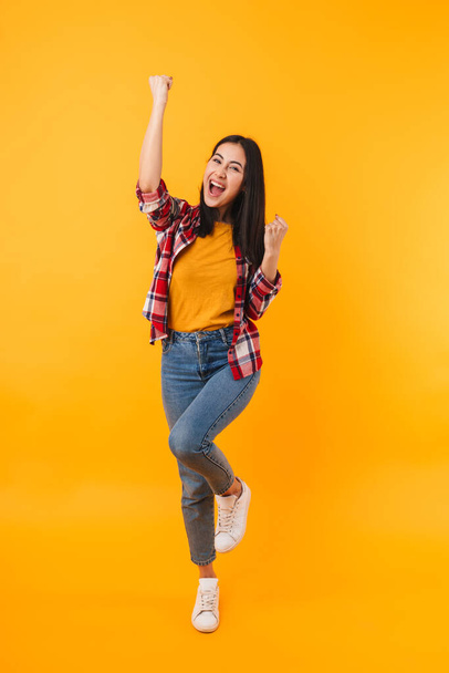 Photo of excited young woman smiling and making winner gesture isolated over yellow background - Zdjęcie, obraz