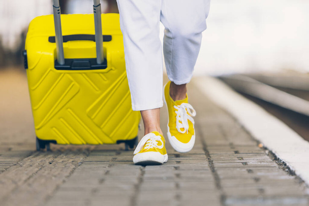 kobieta z żółtą walizką na kółkach przechodząca obok stacji kolejowej - Zdjęcie, obraz