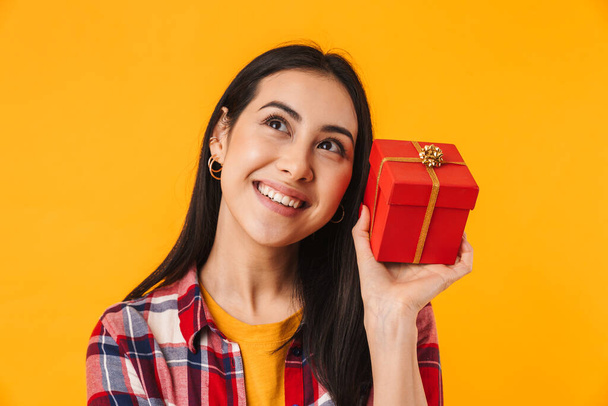 Photo of happy young woman smiling and holding gift box isolated over yellow background - Valokuva, kuva