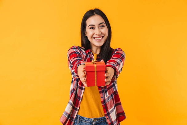 Photo of happy young woman smiling and holding gift box isolated over yellow background - 写真・画像
