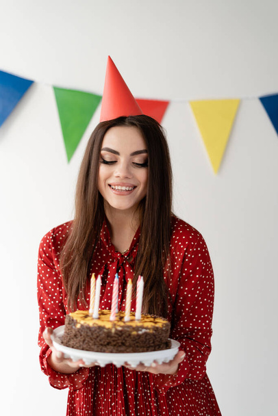 young beautiful girl with a cap on her head holds a beautiful cake in her hands. Holiday birthday. Candles for the holiday. Happiness in the eyes. Place for text - Φωτογραφία, εικόνα
