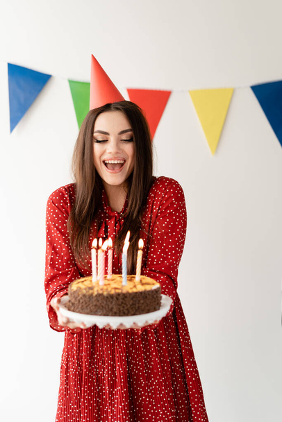 Happy Birthday Celebration. Beautiful stylish girl with a good figure holds a cake in her hands. Pretty smile. Candles on the cake. Fun party place for text. - Zdjęcie, obraz