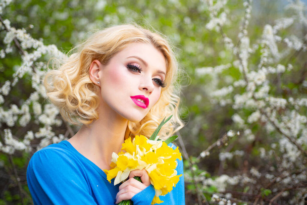 Nahaufnahme Porträt einer schönen jungen Frau mit lockigem blonden Haar, perfekter Haut und schönem Make-up in einem rosa floralen Sommergarten. - Foto, Bild