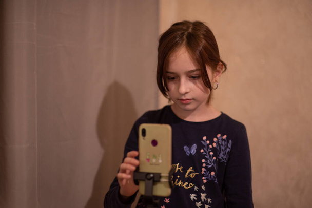 Jovem feliz tomando selfie no fundo branco. Rapariga faz um vídeo de si mesma com um monopod ou selfie stick. Blogueiro. Vlog. A menina faz vídeos para a Internet ou redes de Internet. Retrato
 - Foto, Imagem