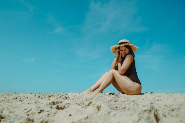 kobieta na plaży piasku w czarnym stroju kąpielowym błękitne niebo na tle. letnie wakacje - Zdjęcie, obraz