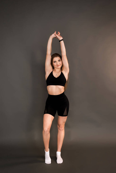 Fitness girl doing a stretch on a dark background. - Фото, изображение