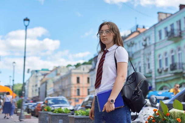 Portrait girl student teenager in glasses tie white T-shirt with backpack. Background city street, copy space - Foto, imagen