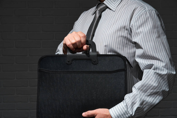 Businessman closeup portrait, he standing and posing with briefcase, dark wall background - Фото, изображение