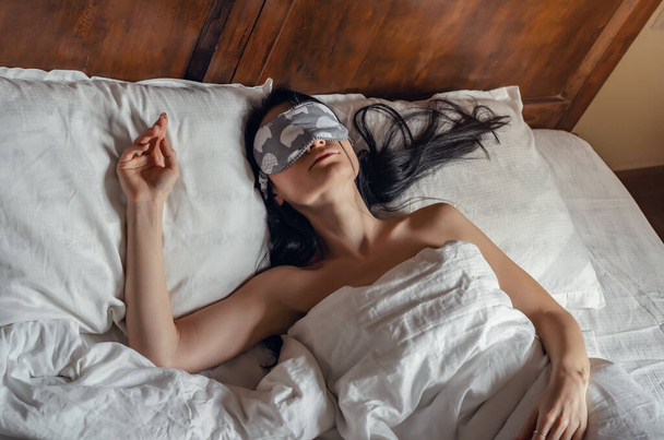 Femme dormant dans un masque de sommeil au lit avec draps blancs sur lit vintage
 - Photo, image