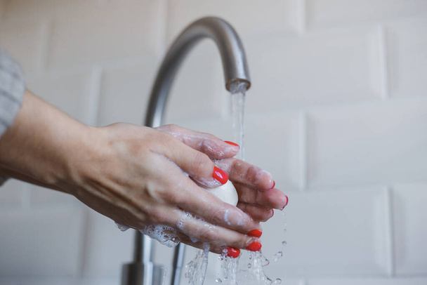 Gros plan de jeune femme se lave les mains avec du savon pour prévenir l'infection par le coronavirus. Les mains avec des ongles rouges sont soigneusement lavées pour maintenir l'hygiène. Sécurité des virus. Concept d'arrêt Covid-19
. - Photo, image