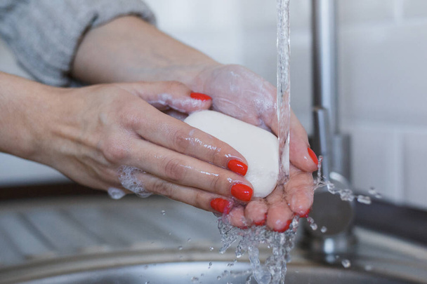 Lähikuva nuori nainen pesee kätensä saippualla estää sepelvaltimotautitartunta. Kädet punaisilla kynsillä pestään perusteellisesti hygienian ylläpitämiseksi. Virusturvallisuus. Covid-19 stop-konsepti
. - Valokuva, kuva