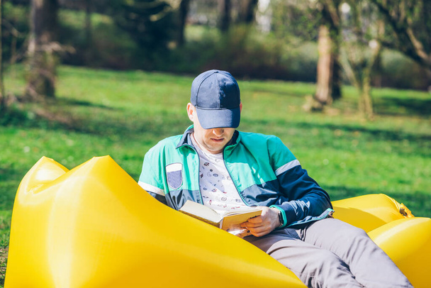 boek reading concept. man in stadspark op opblaasbare matras. lente zonnige dag - Foto, afbeelding
