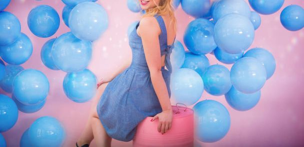 Young beautiful blonde Caucasian girl in a blue denim sundress celebrates with many blue balls on her birthday - Фото, изображение