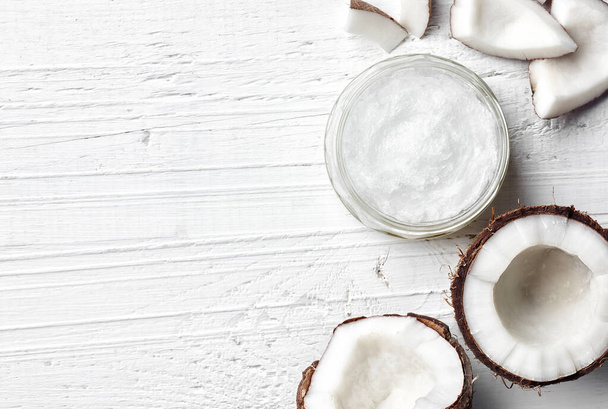 Jar of coconut oil and fresh coconut on white wooden background, top view - Photo, Image