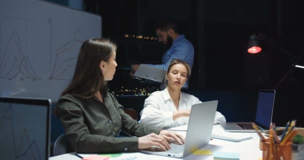 Caucasian good looking male and female colleagues having business meeting in office late at night. Man and two women working with documents and talking in evening. - Materiał filmowy, wideo