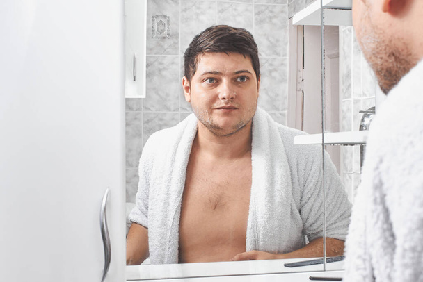 Yüzünde sabun olan beyaz önlüklü bir adam banyo aynasına bakıyor.. - Fotoğraf, Görsel