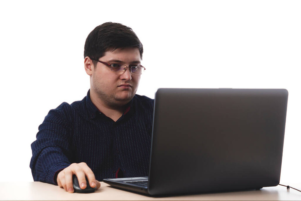 Jeune homme vêtu d'une chemise bleu foncé derrière un ordinateur portable en lunettes pour le bureau, vision d'affaires sur fond blanc. isoler. espace de copie
 - Photo, image