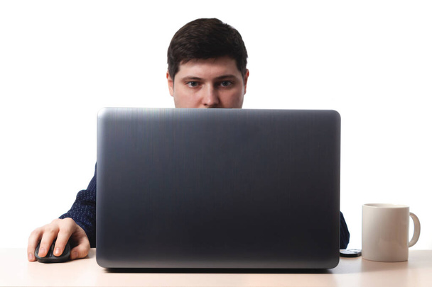 Egy fiatal fickó sötétkék ingben gépel egy laptop billentyűzetén egy iroda mellett, egy üzleti csésze kávé fehér háttérrel. elkülöníteni. másolás helye - Fotó, kép