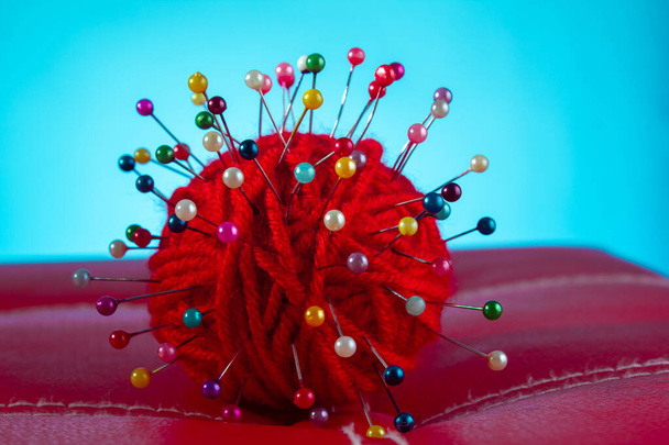a red skein of thread stuck a lot of needles on red leather on a blue background. close up copy space - Photo, Image