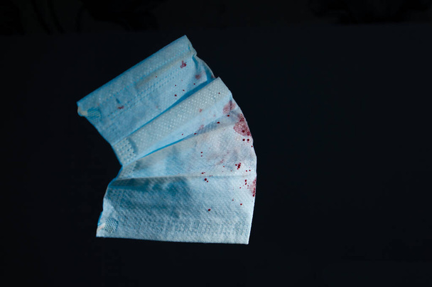 maschera di garza medica blu con sangue su uno spazio di copia di sfondo scuro. vicino
 - Foto, immagini