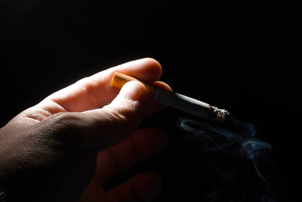 mano tenere una sigaretta in fiamme in fumo su uno spazio di copia di sfondo nero. vicino
 - Foto, immagini