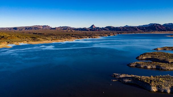 澄んだ青い空と水、茶色の丘と紫色の山々、そして美しい砂漠の風景を持つビル・ウィリアムズ川のアリゾナ州アラモ湖州立公園の空中ドローンビュー - 写真・画像